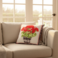 Beige sofa with a decorative pillow featuring red flowers, surrounded by large windows with a view of greenery.